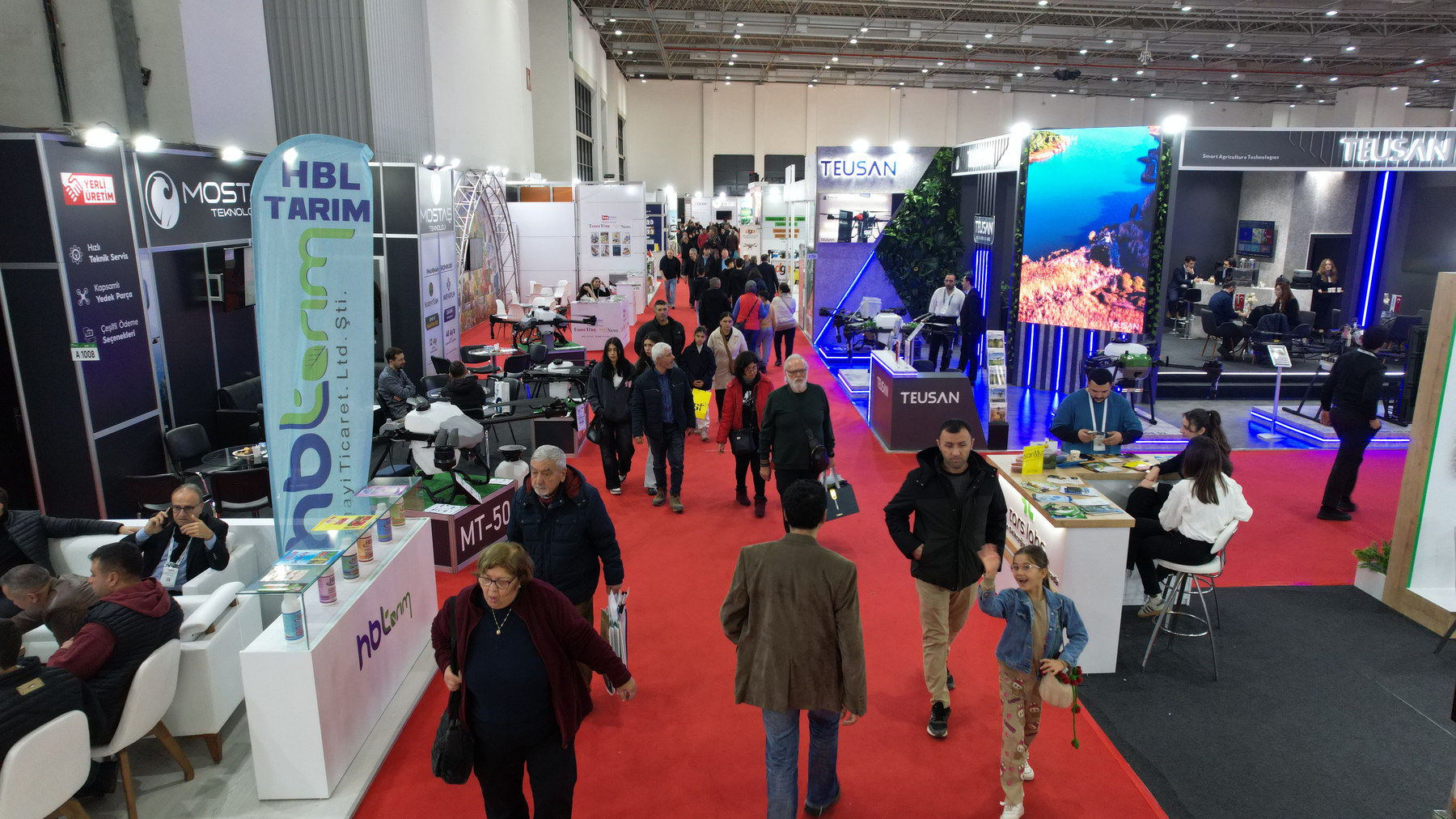 AGROEXPO fuar koridoru; halı serili aks boyunca stantlar arasında ilerleyen ziyaretçiler